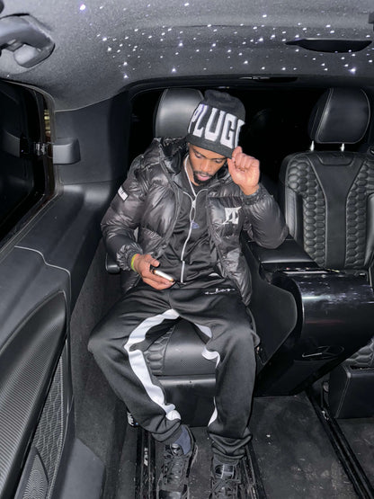 Man wearing Plug Calling Groundwork Beanie and black outfit inside a luxury car.