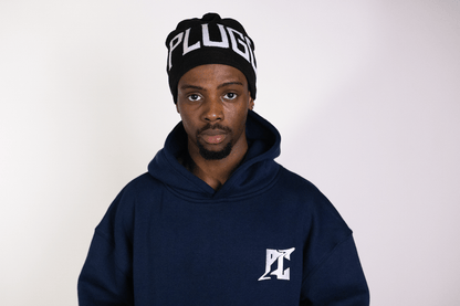 Person wearing Plug Calling Black Groundwork Beanie with distinctive wrap-around logo, showcasing empowering unisex clothing.